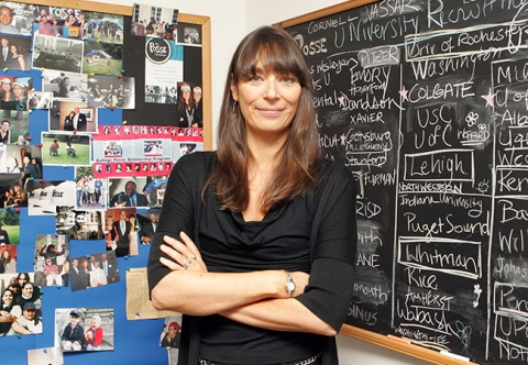 Deborah Bial standing with arms crossed in front of a chalkboard with writing and corkboard with photos